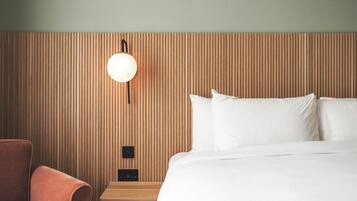 A hotel room with a wooden headboard, a bed with white linens, a round wall-mounted light, and a small wooden nightstand.