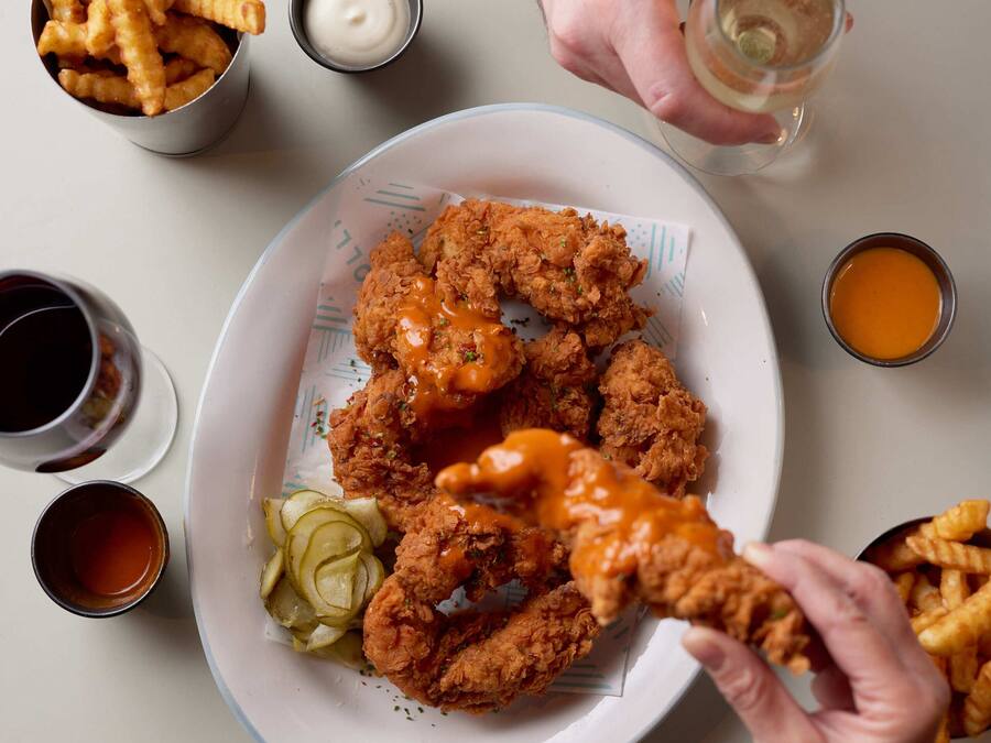 Een bord met gefrituurde kip en friet met dipsausjes, een glas witte wijn en een kop koffie op een tafel.