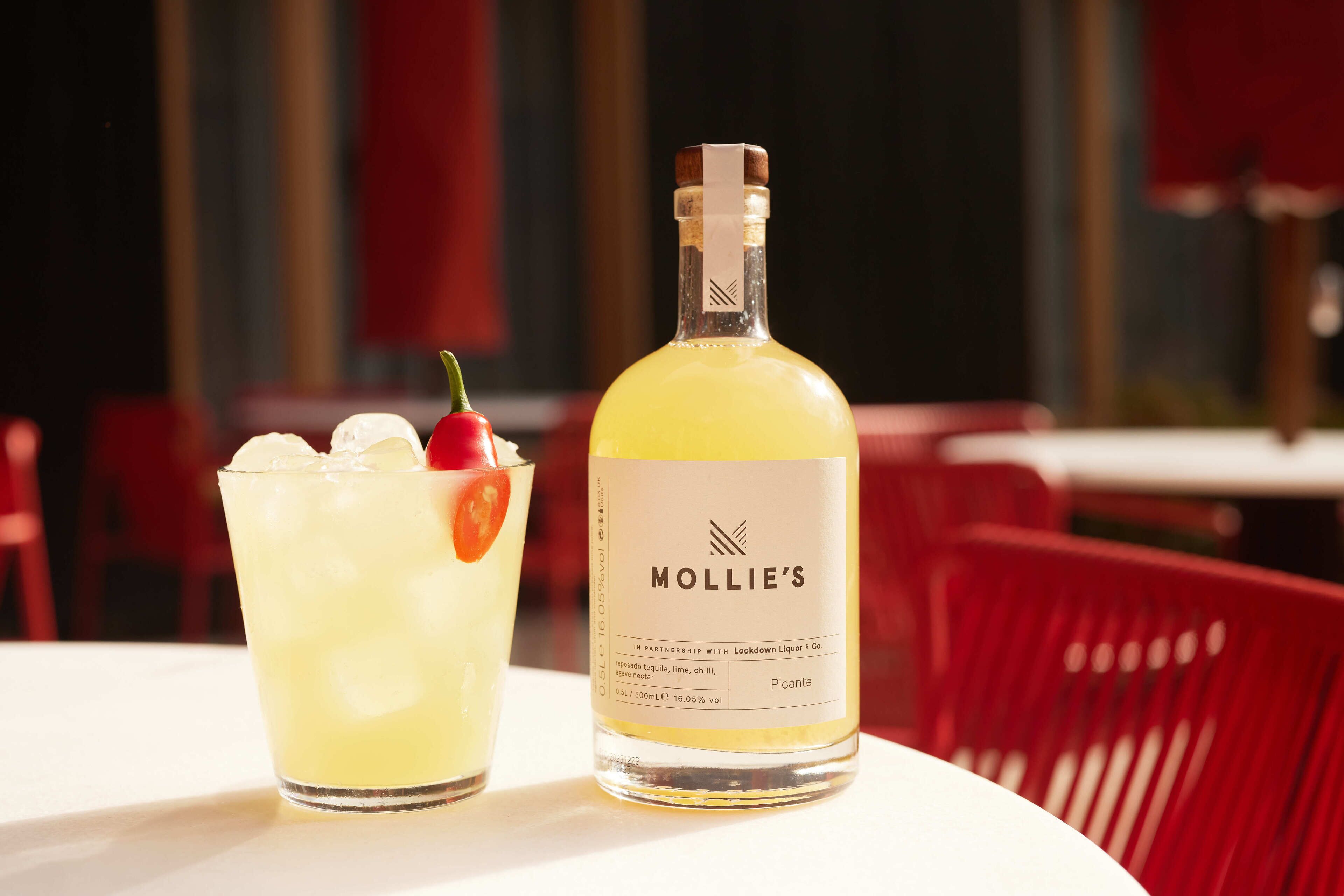 A bottle of Mollie's Picante tequila and a glass of margarita on a table.
