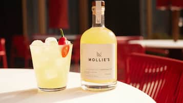 A bottle of Mollie's Picante tequila and a glass of margarita on a table.