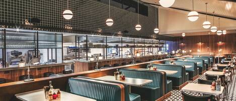 Un restaurante con cabinas y mesas, una cocina al fondo y un suelo estampado.