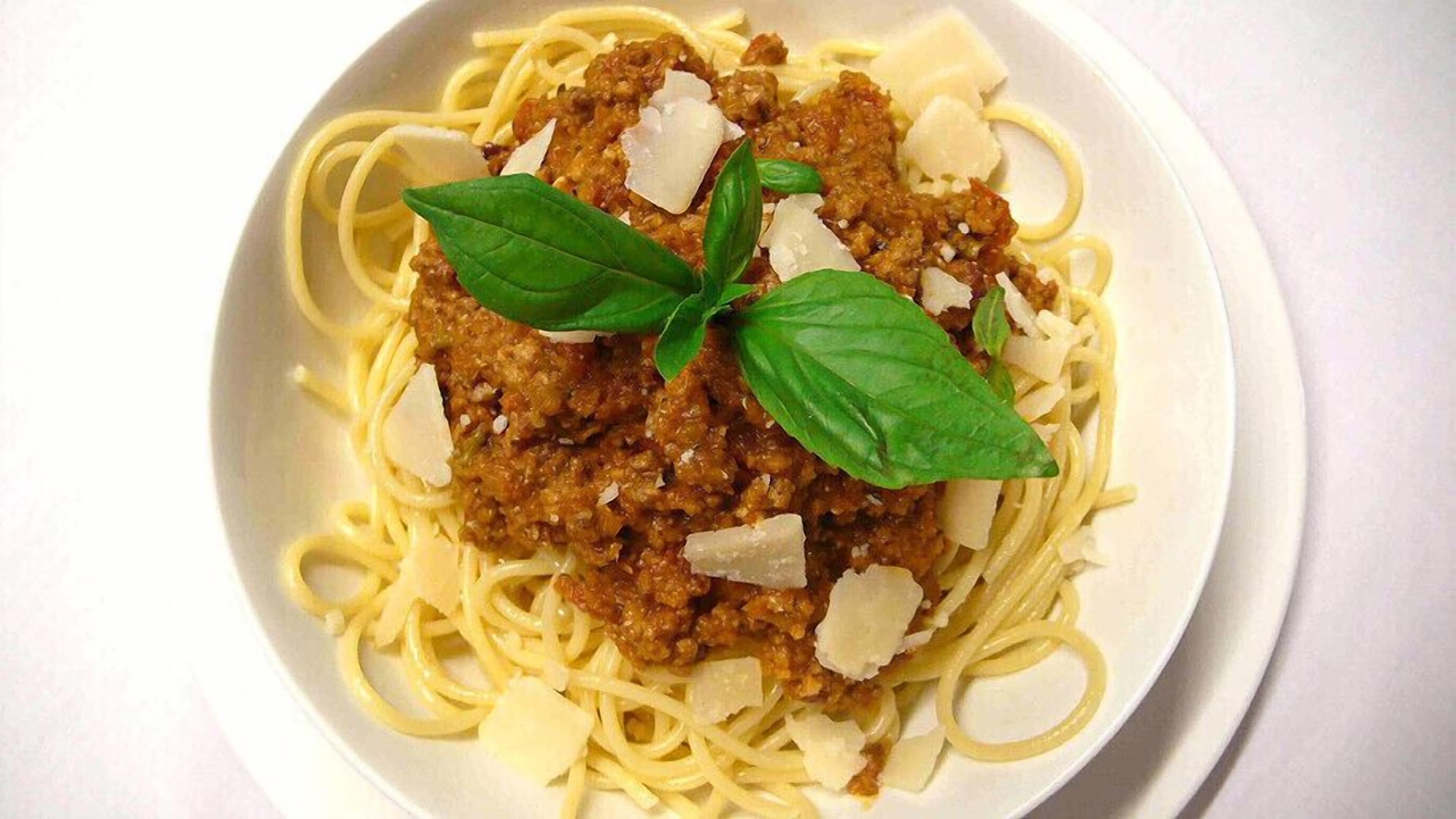 Eine Schüssel Spaghetti mit Fleischsoße und geriebenem Käse, garniert mit Basilikumblättern.