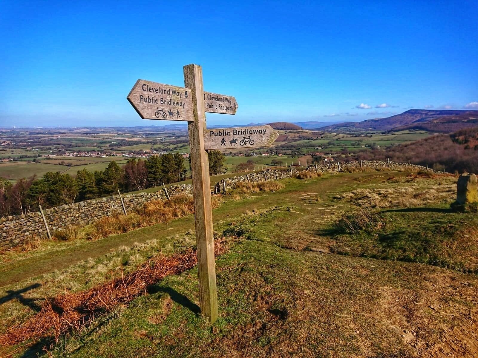 A wooden signpost with directions for Cleveland Way, Public Bridleway, and Public Footpath.