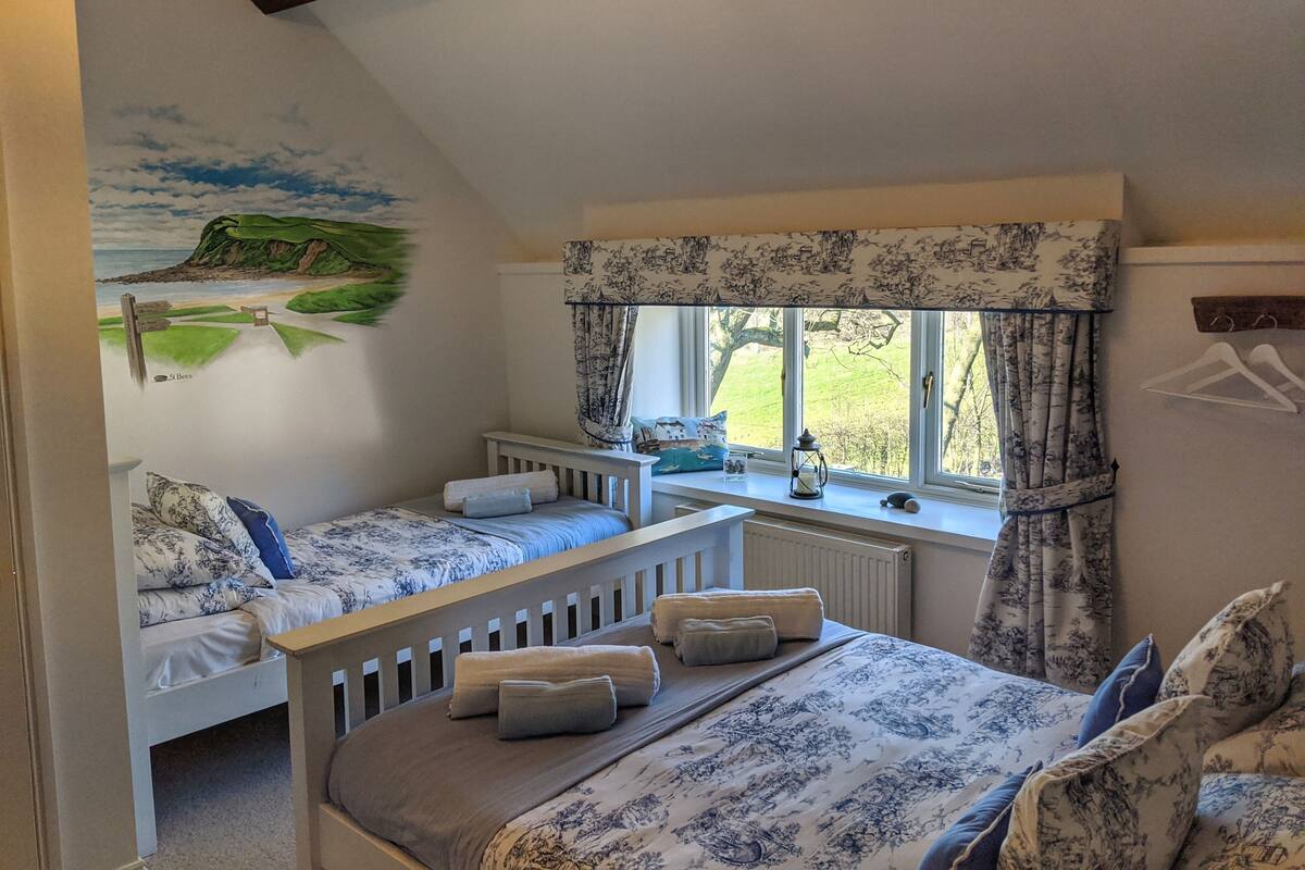 Un dormitorio con dos camas individuales, una cama grande, una ventana con cortinas, un radiador y un mural en la pared.
