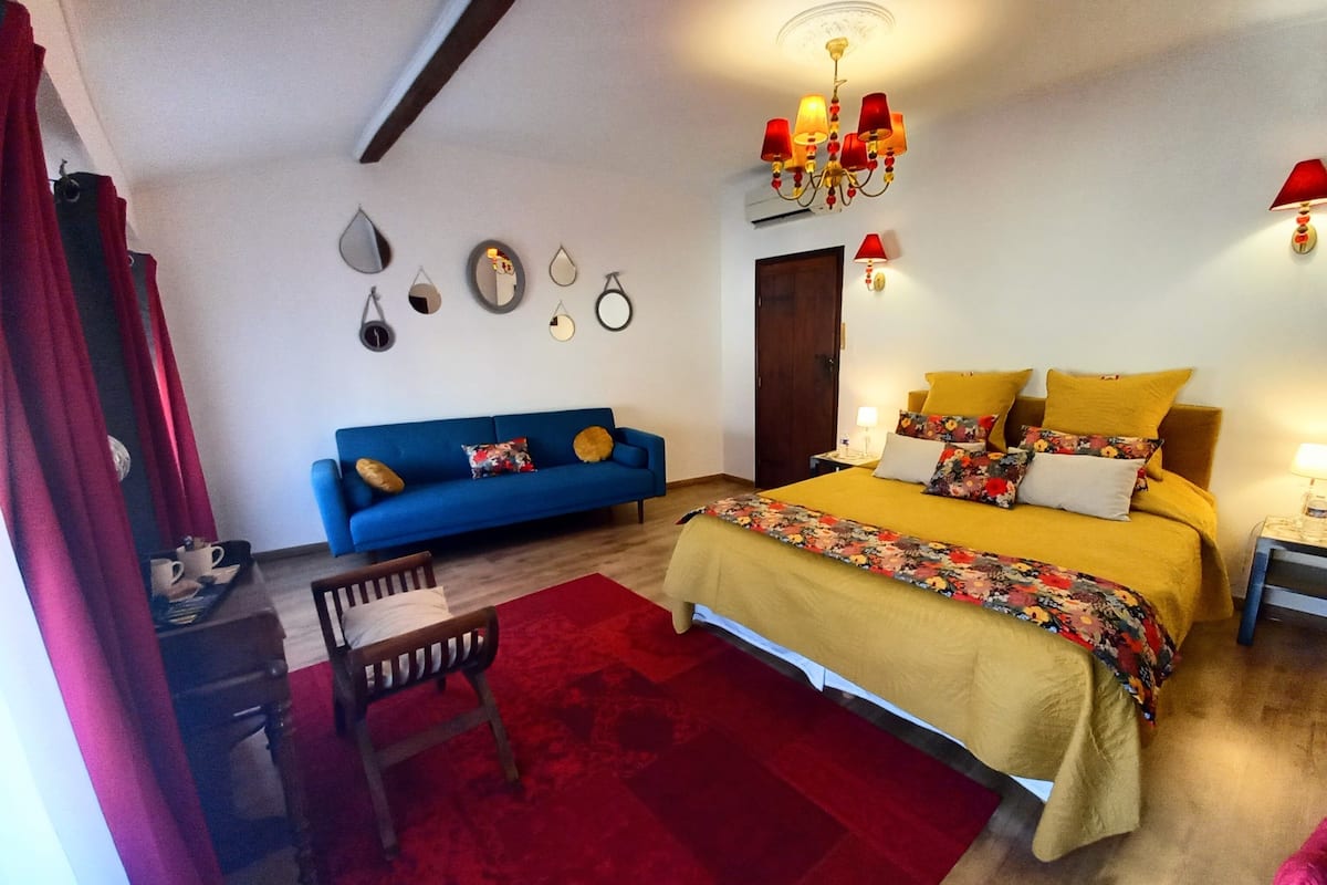 Une chambre à coucher avec un lit, un canapé bleu, une chaise en bois, un tapis rouge et un lustre.