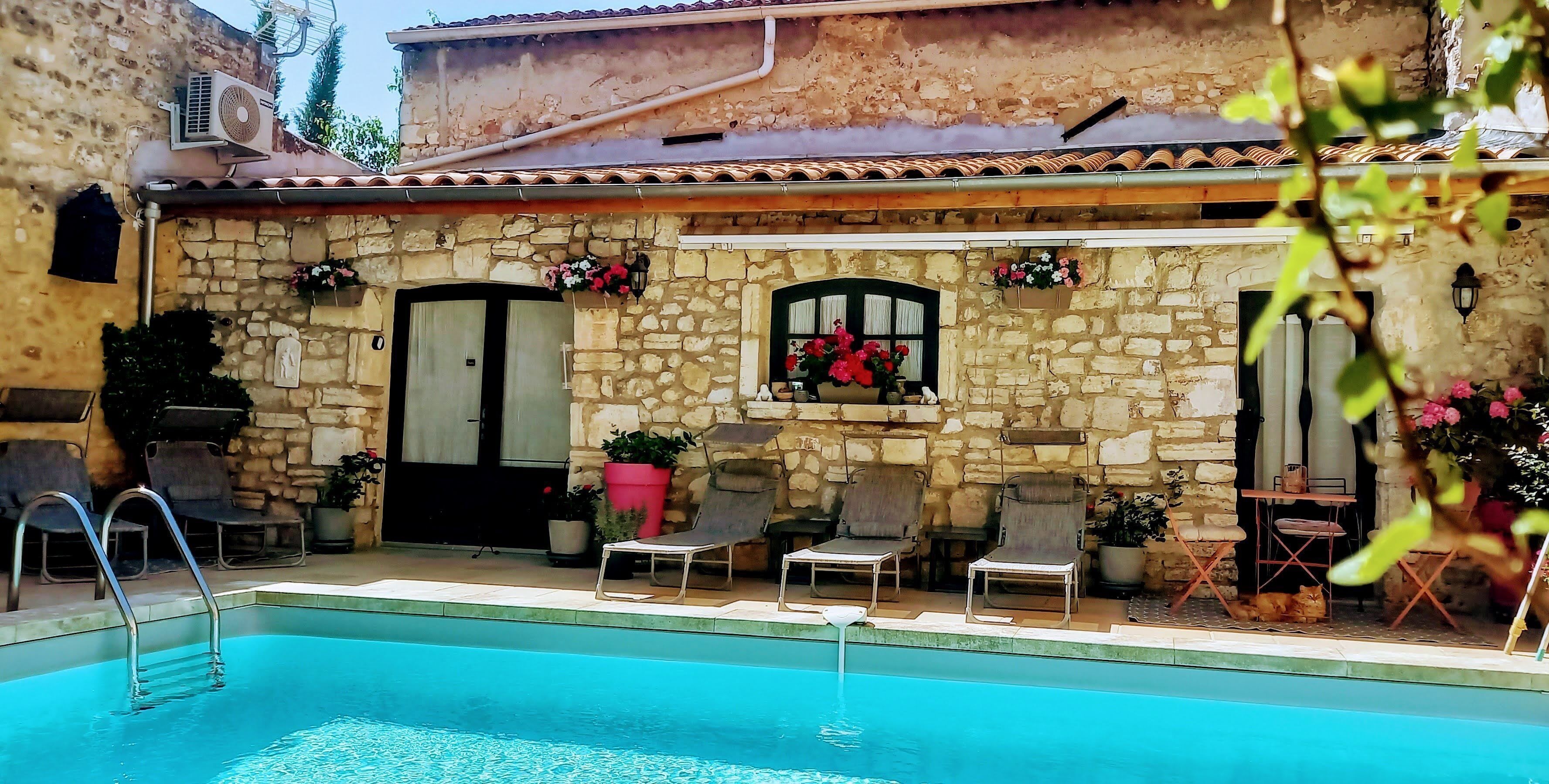 A stone building with a pool, outdoor seating, and a cat.