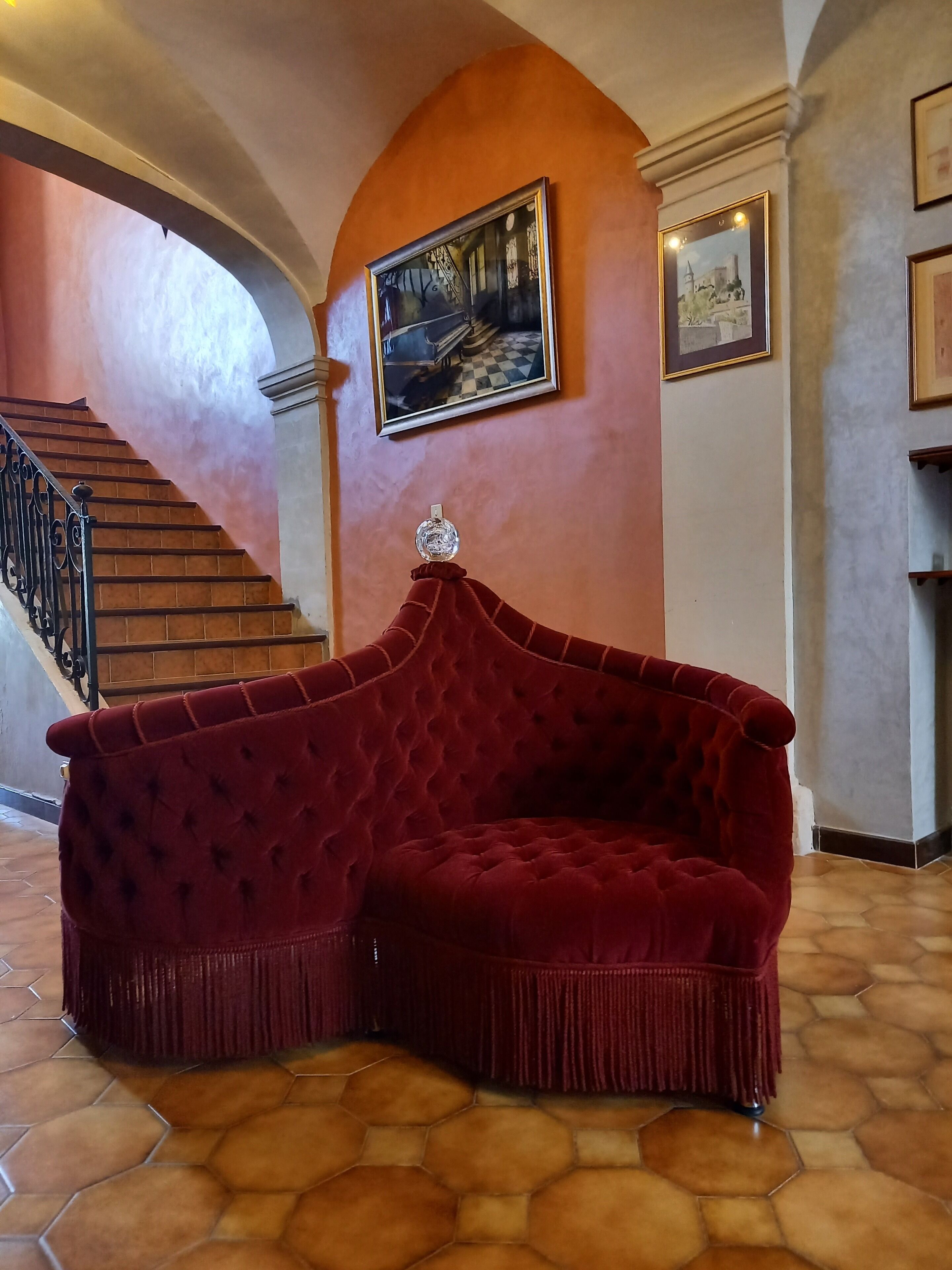 A red velvet sofa in a lobby with a staircase and a painting on the wall.