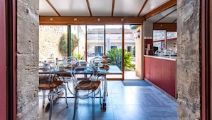 Un espace repas offrant une vue sur un bâtiment traditionnel, un comptoir où sont présentés des produits alimentaires et un mur en pierre.
