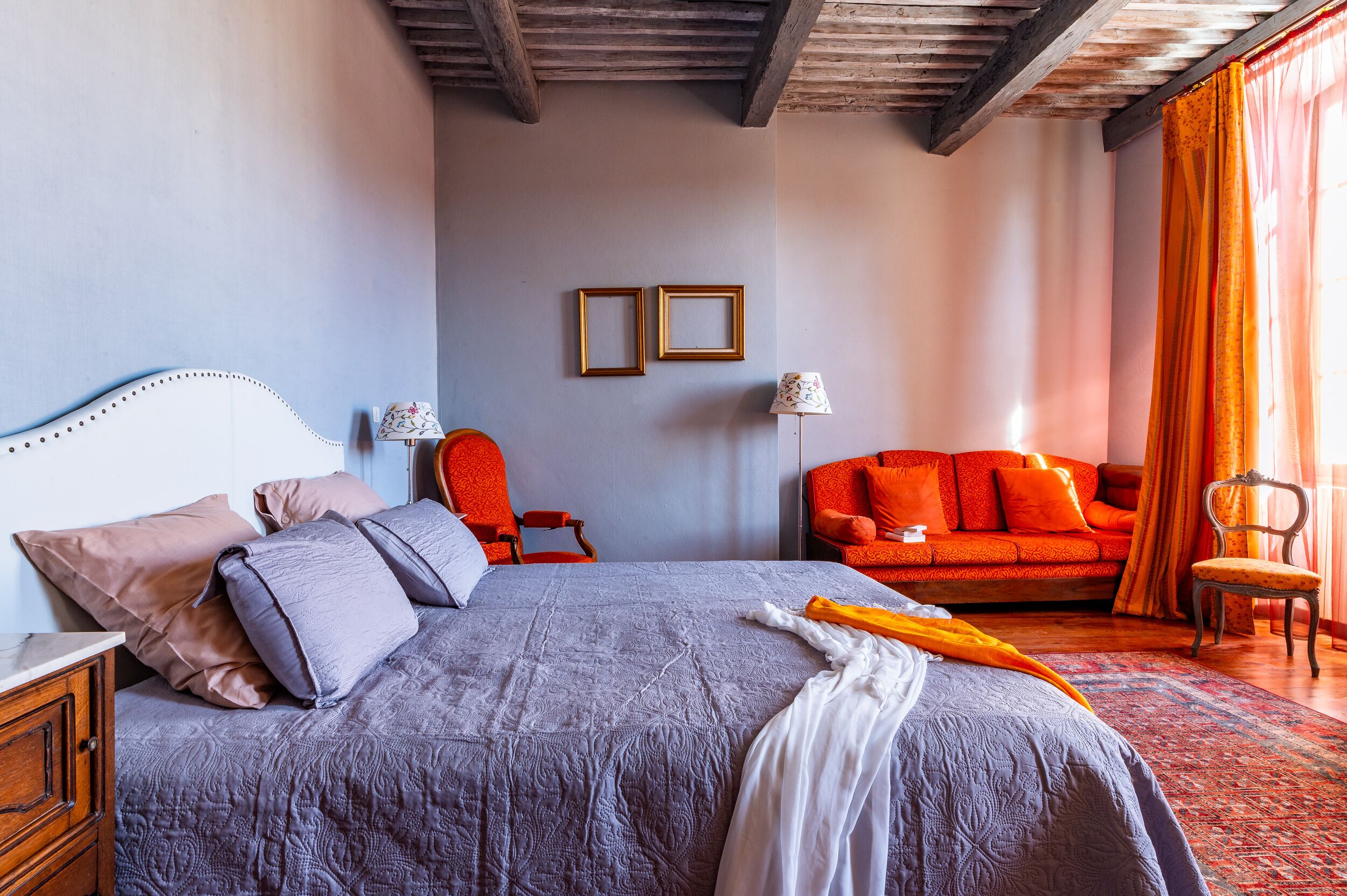 Un dormitorio con una cama, un sofá rojo, una silla y dos cuadros colgados en la pared.