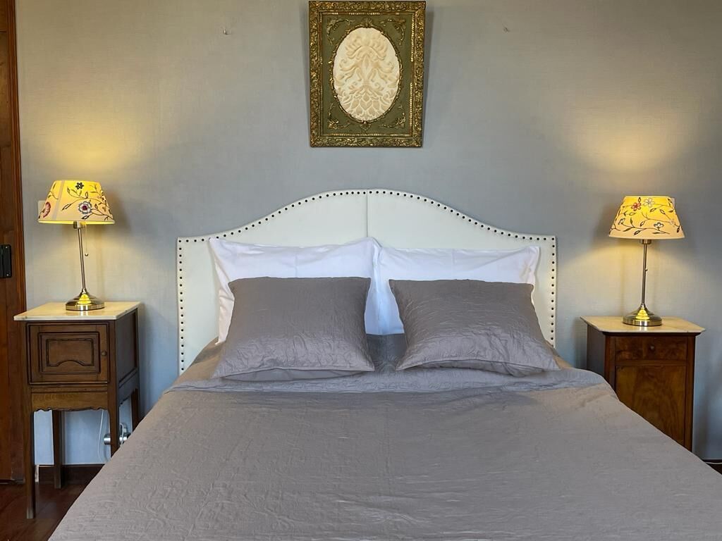 Una cama bien hecha con cabecera blanca, dos mesitas de noche con lámparas y un adorno decorativo sobre la cama.