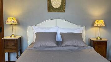 Una cama bien hecha con cabecera blanca, dos mesitas de noche con lámparas y un adorno decorativo sobre la cama.