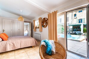 Een slaapkamer met een bed, een rieten stoel, een raam en uitzicht op een buitenzwembad.