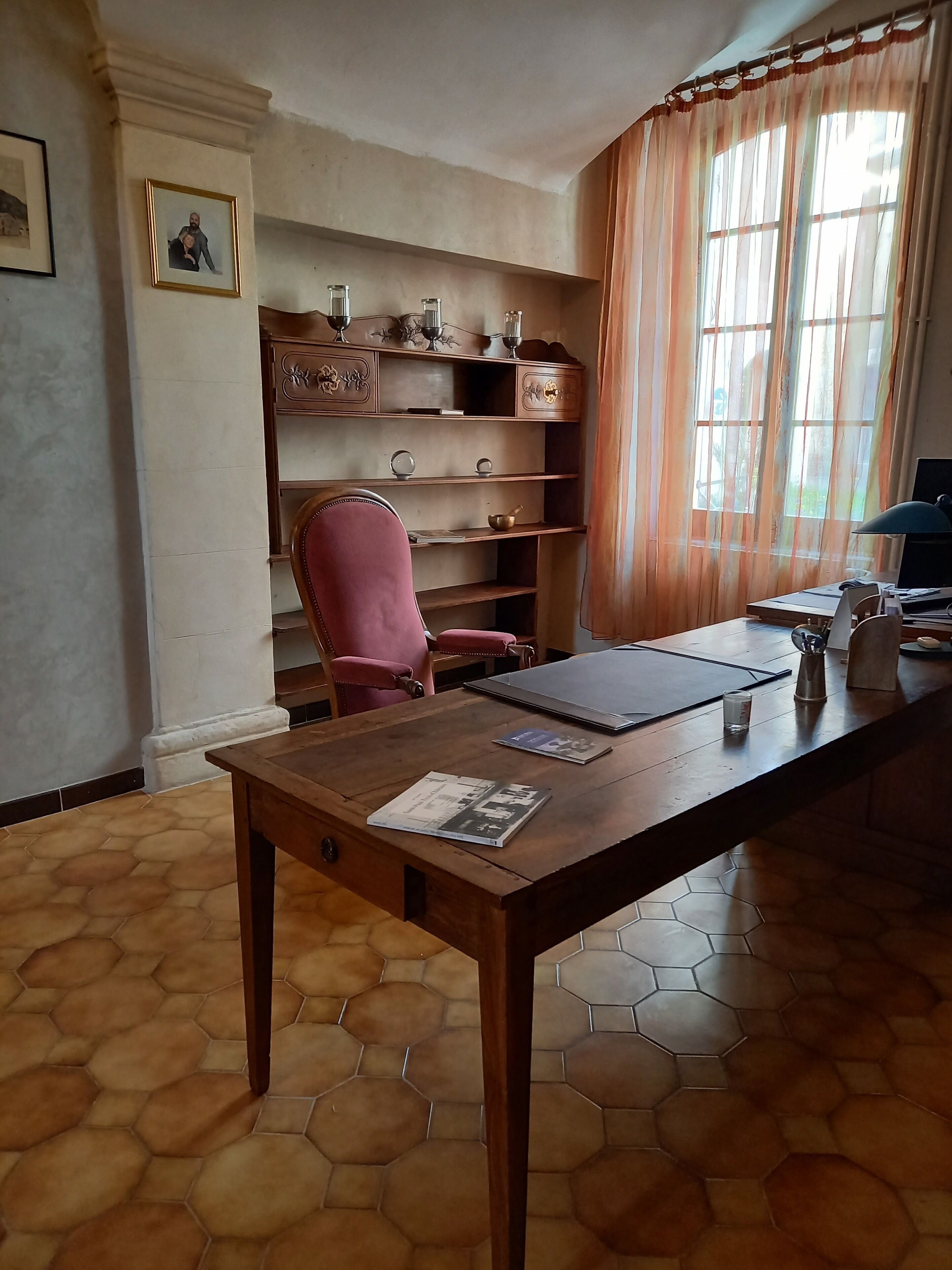 A room with a wooden desk, a chair, a bookshelf, and a window with curtains.
