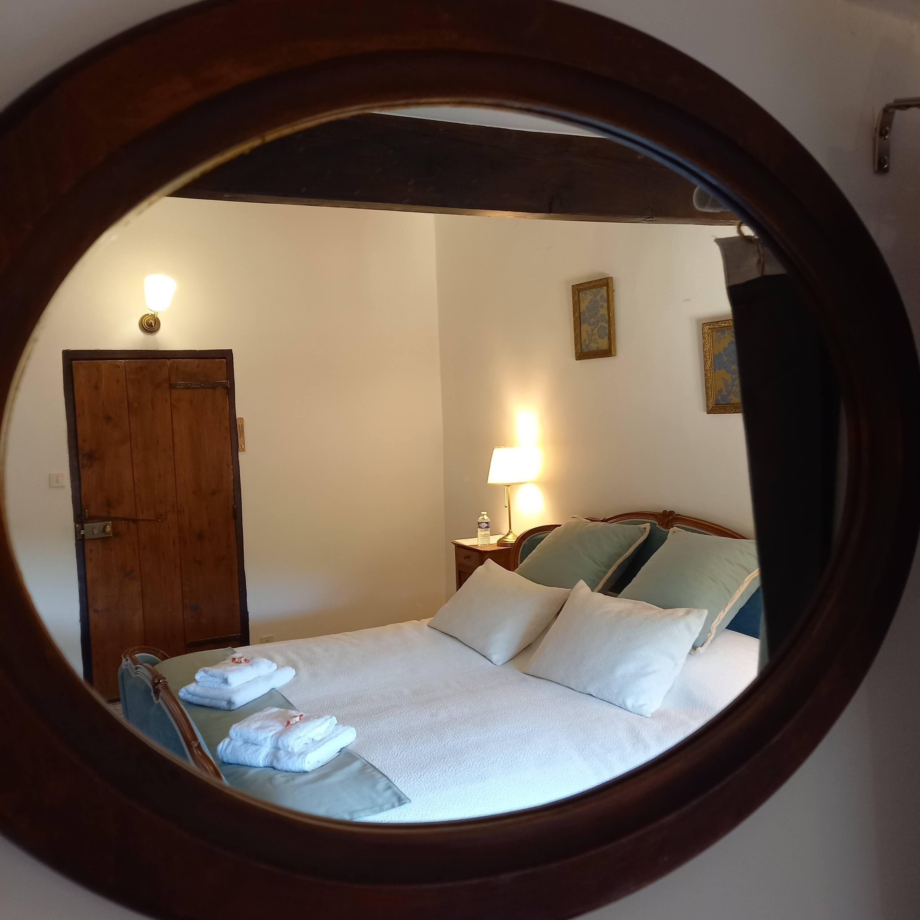 Ein runder Spiegel, der ein Schlafzimmer mit Bett, Kissen, einem Nachttisch, einer Lampe und einer Tür zeigt.
