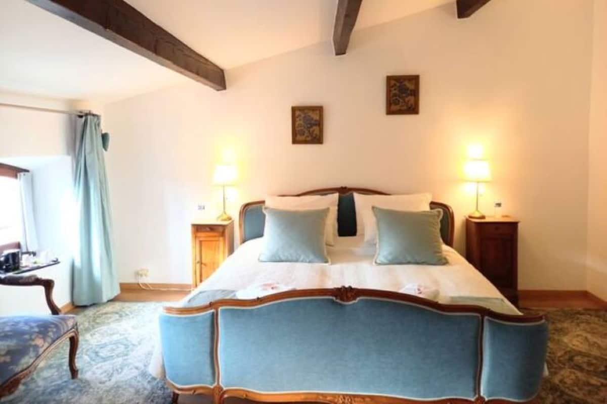 Une chambre à coucher avec un grand lit, deux tables de chevet avec des lampes, une chaise et une fenêtre avec des rideaux.
