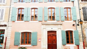 Un bâtiment doté de nombreuses fenêtres et d’une porte centrale, présentant un style architectural traditionnel avec des volets et un toit en tuiles.