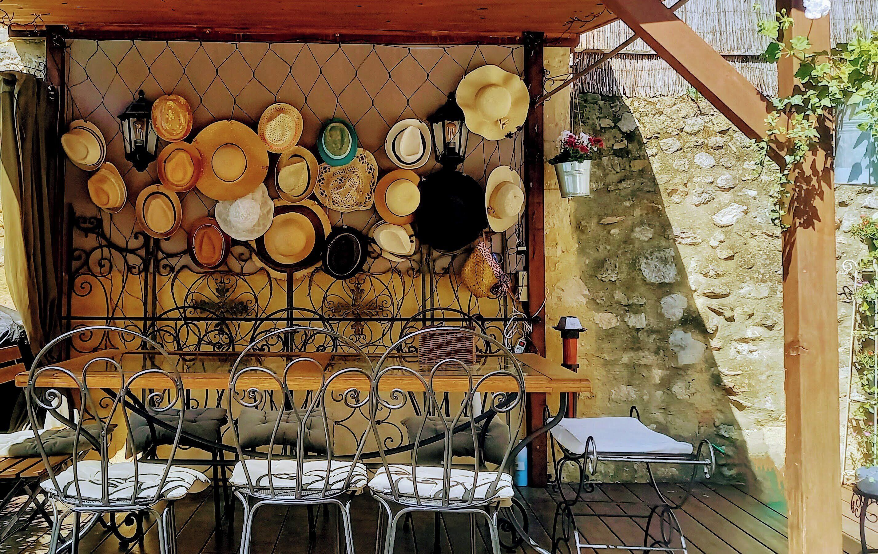 Eine Terrasse mit Tisch und Stühlen, ein Metallzaun mit Hüten und Tellern, und eine Steinmauer.