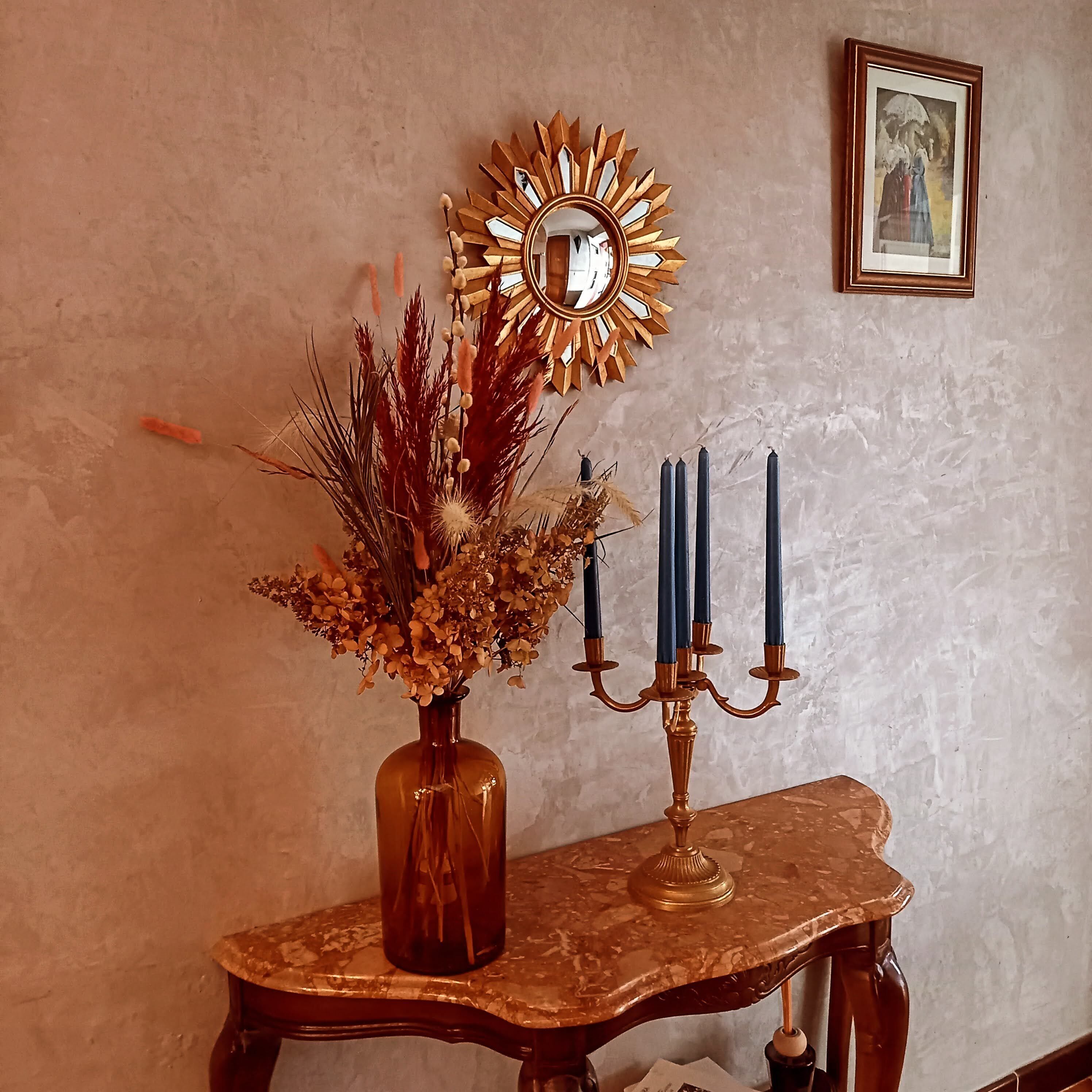 Una mesa con un jarrón de flores secas y un candelabro con velas.