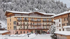 A multi-story hotel with balconies, a ski resort in the background, and a snowy landscape. - Familienhotel Vent (Soelden)