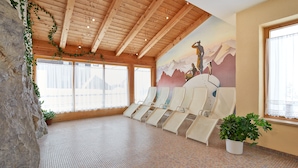 A spa room with wooden ceiling beams, a mural of mountains, and a row of sun loungers. - Familienhotel Vent (Soelden)