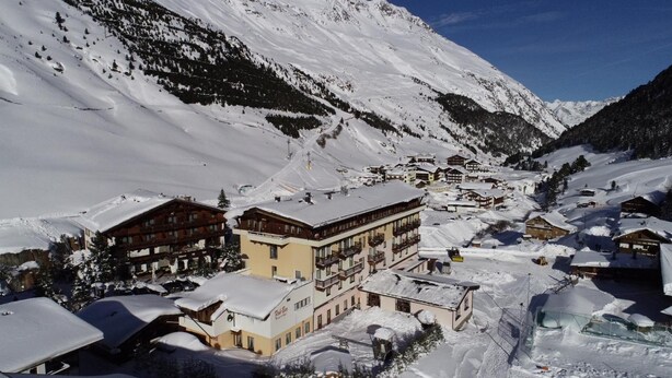 A snow-covered mountain village with traditional wooden buildings, a ski lift, and a clear blue sky. - Familienhotel Vent (Soelden)