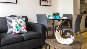A modern living room with a sofa, chairs, a dining table, and a kitchen in the background. - Tudors eSuites Birmingham Canalside Apartments (Birmingham)