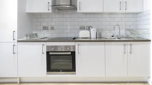 A modern kitchen with white cabinets, a built-in oven, a stainless steel range hood, and a tiled backsplash. - Tudors eSuites Birmingham Canalside Apartments (Birmingham)