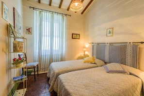 A bedroom with two beds, a chair, a shelf with items, and a window with curtains. - Verdidea - Podere del Mezzadro (Radicofani)