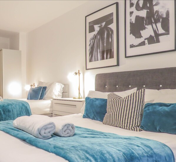 Un dormitorio ordenado con una cama, mesitas de noche y dos cuadros enmarcados en la pared.