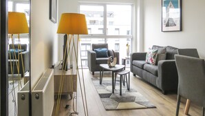 A modern living room with a sofa, armchairs, a coffee table, and a floor lamp. - Tudors eSuites Birmingham Canalside Apartments (Birmingham)