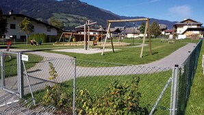 A playground with swings and slides, surrounded by a fenced area with a walking path.