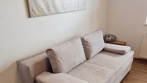 A modern living room with a beige sofa, a large abstract painting on the wall, and a wooden floor.