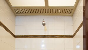 Une douche avec une lucarne au plafond, des murs recouverts de carreaux blancs et un sol marron.