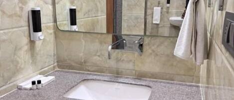 Un baño con lavamanos de encimera de granito, un espejo, un perchero para toallas y un dispensador de jabón.