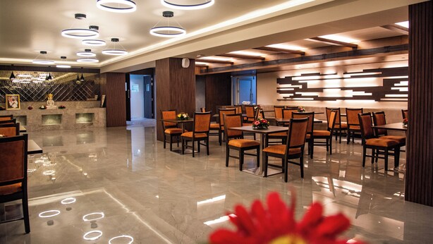 Un hall d’hôtel spacieux au design moderne, avec un sol en marbre poli, de nombreuses tables à manger accompagnées de chaises et des luminaires contemporains.