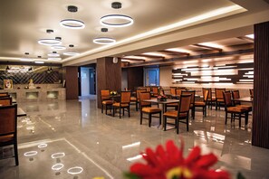 A spacious hotel lobby with a modern design, featuring a polished marble floor, multiple dining tables with chairs, and contemporary lighting fixtures. - Siara Styles Amba Suites (Gandhinagar)