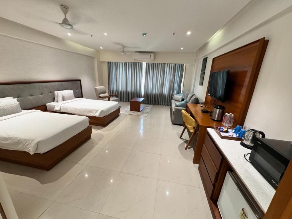 A hotel room with two beds, a desk, a chair, a television, and a minibar.