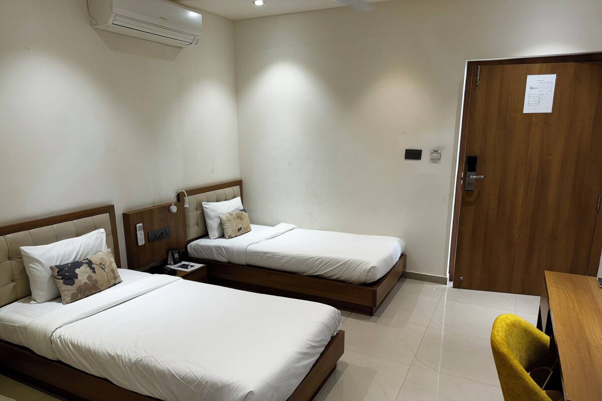 A hotel room with two beds, a wooden desk, a chair, an air conditioning unit, and a door with a lock.