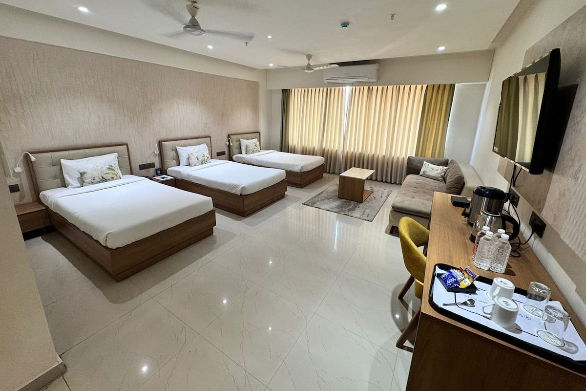 A hotel room with three beds, a sofa, a coffee station, and a TV mounted on the wall.