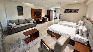 Une chambre d’hôtel moderne équipée d’un canapé, de deux lits simples, d’un bureau, d’une chaise et d’une télévision.