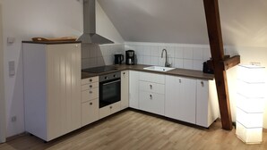 A compact kitchen with white cabinets, a black oven, a stainless steel range hood, and a wooden countertop. - Landhof Potsdam (Potsdam)