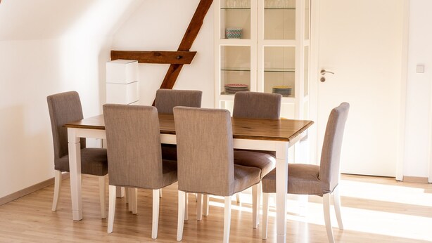 A dining area with a wooden table and six chairs, a white cabinet with glass doors, and a wooden staircase. - Landhof Potsdam (Potsdam)