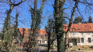 A courtyard with trees, a red-tiled roof building, and a white building with a green door. - Landhof Potsdam (Potsdam)
