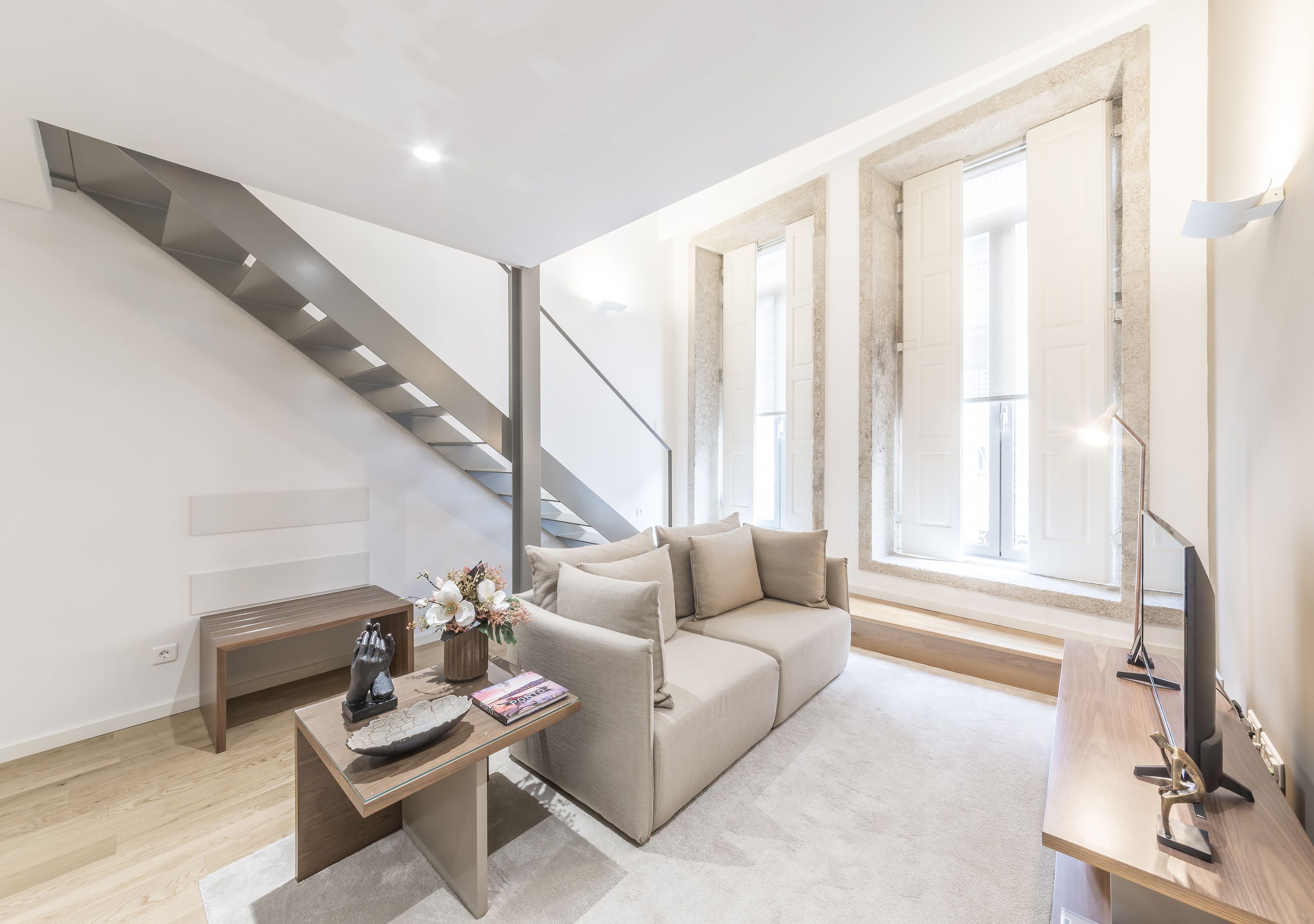 A modern living room with a sofa, a coffee table, a small desk, and a staircase.