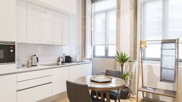 Una cocina moderna con armarios blancos, una mesa de comedor con sillas, una cafetera y una planta.