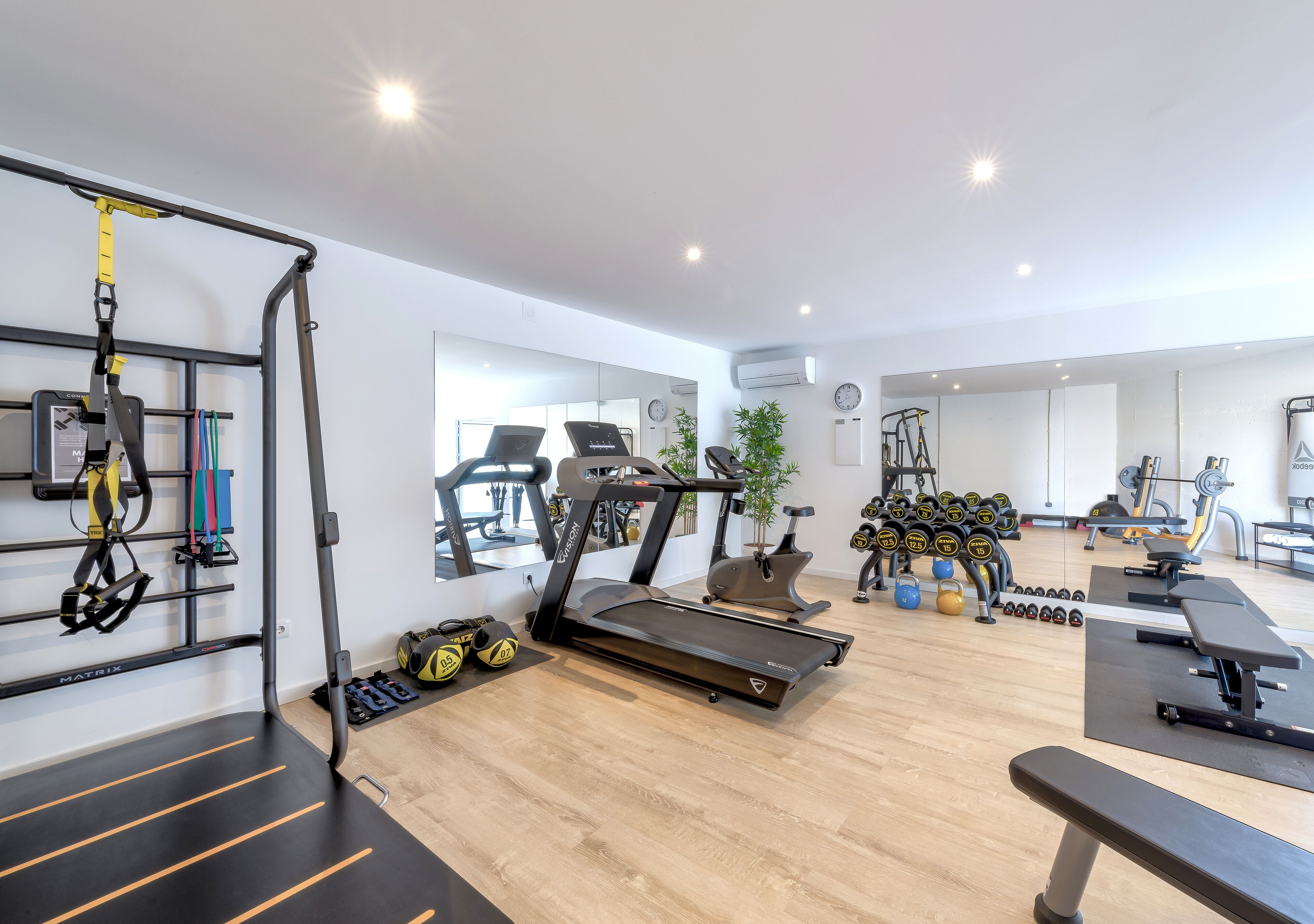 A gym with a treadmill, weight bench, TRX suspension trainer, and various weights.