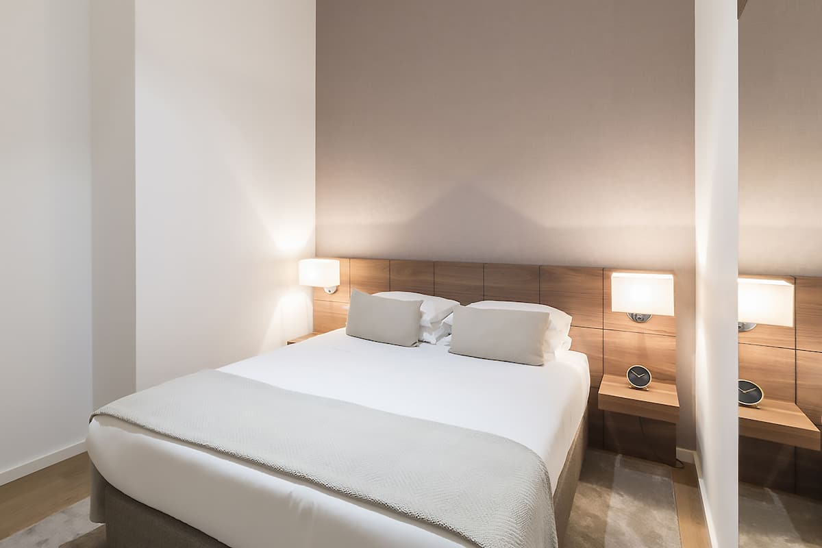 A neatly arranged hotel room with a large bed, two bedside tables with lamps, and a wooden headboard.