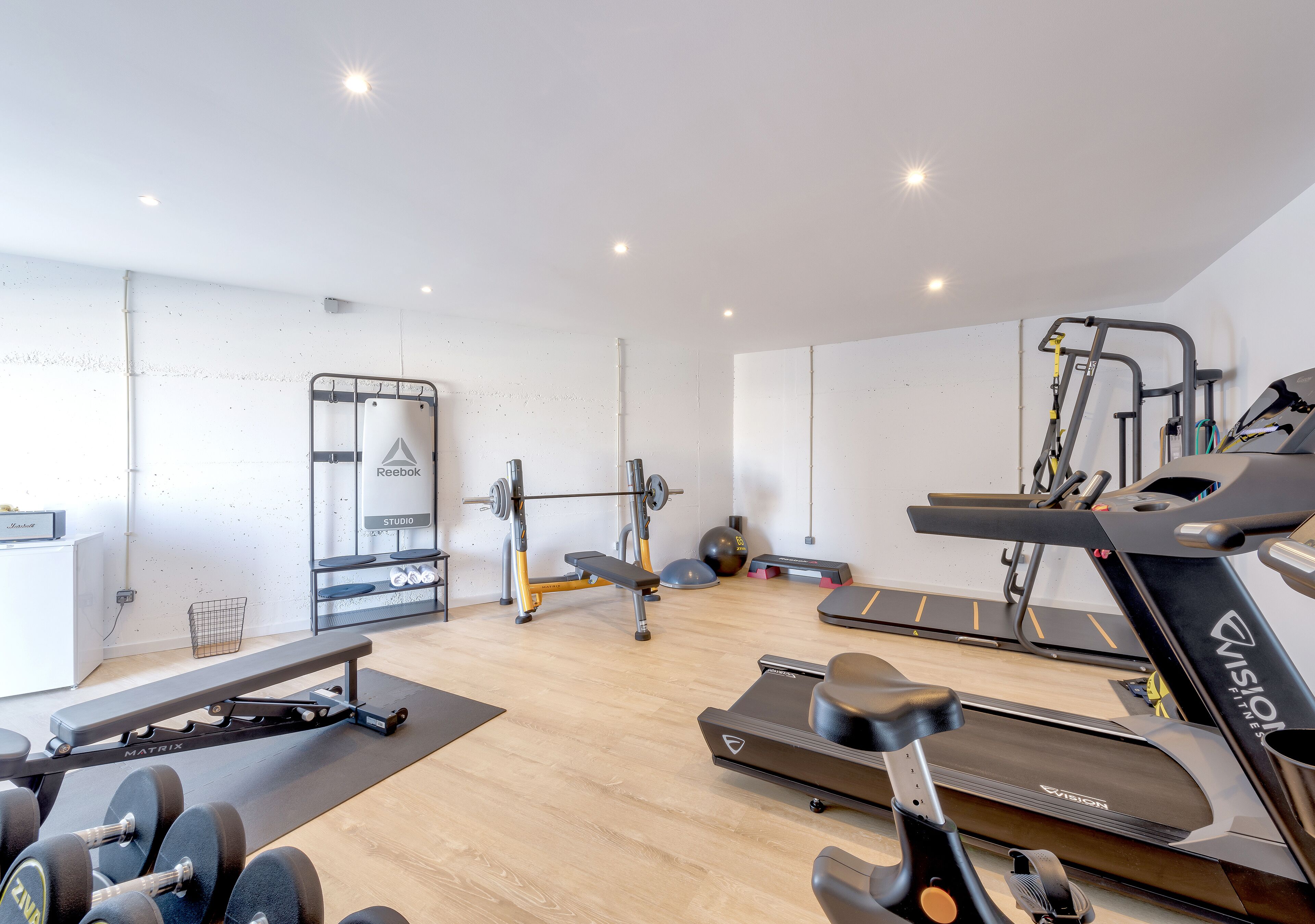 Un gimnasio moderno con cintas de correr, un banco de pesas, mancuernas y una jaula para sentadillas.