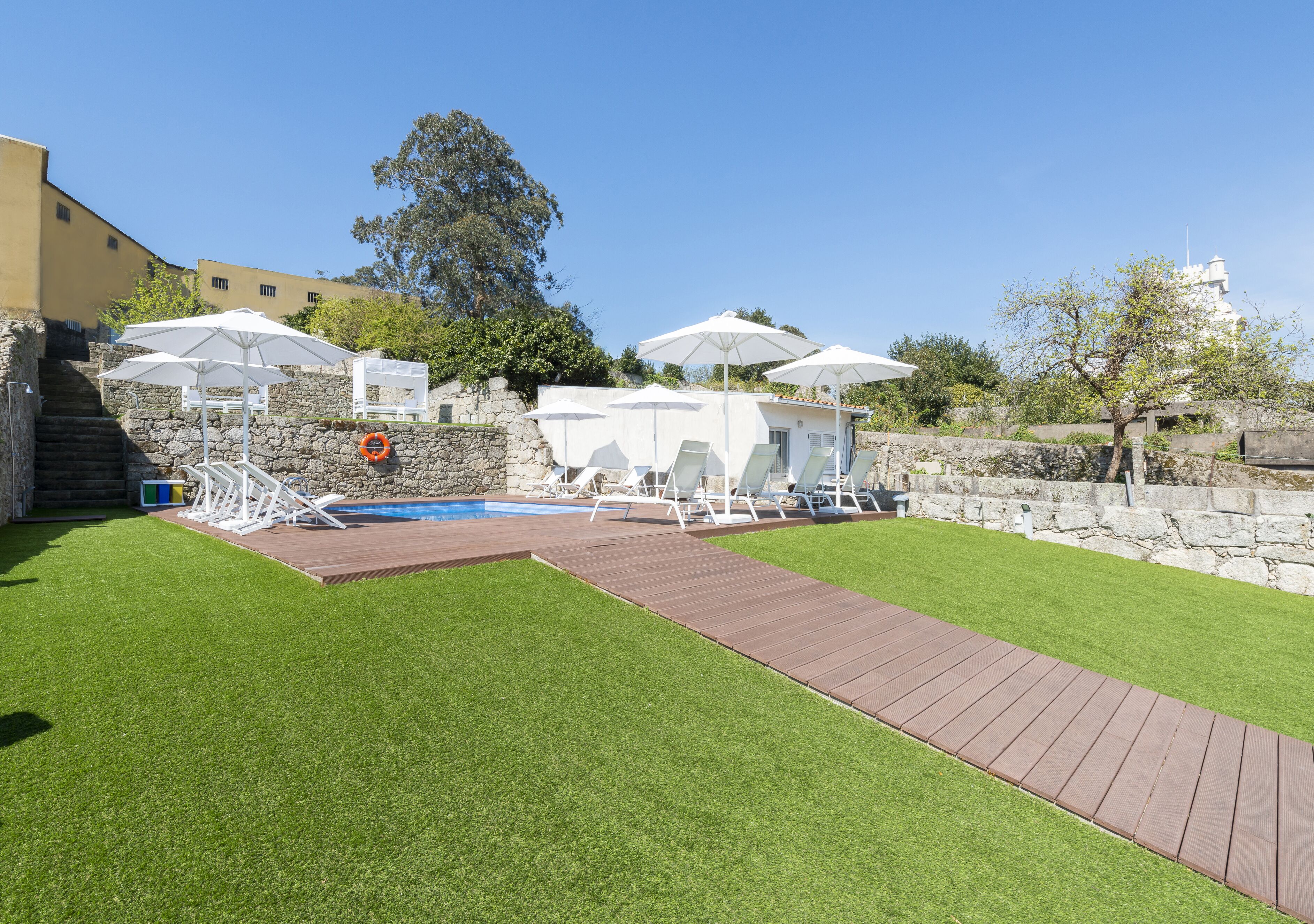 A backyard with a swimming pool, sun loungers, and umbrellas.