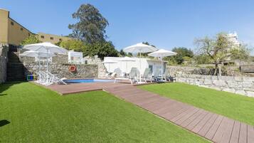 A backyard with a swimming pool, sun loungers, and umbrellas.